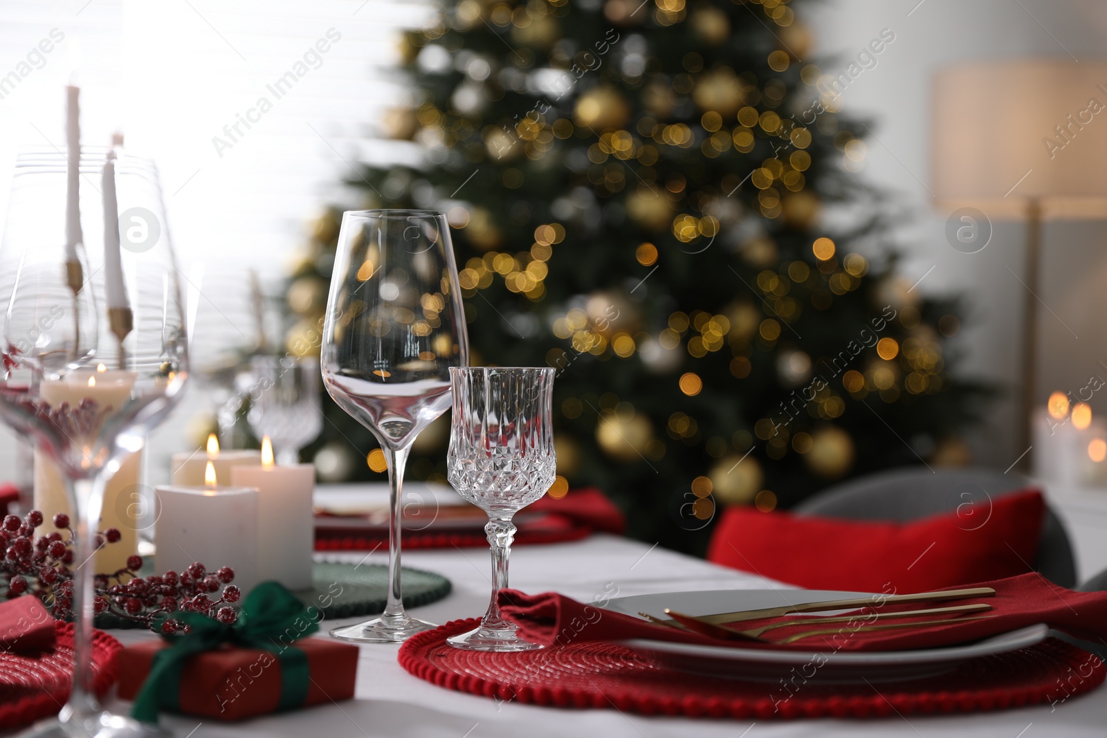 Photo of Christmas table setting with burning candles, gift box and dishware indoors