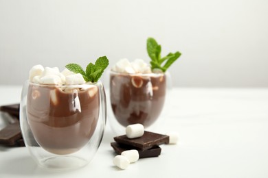 Glasses of delicious hot chocolate with marshmallows and fresh mint on white table. Space for text