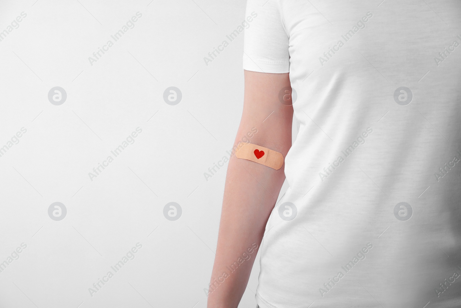 Photo of Blood donation concept. Woman with adhesive plaster on arm against white background, closeup. Space for text