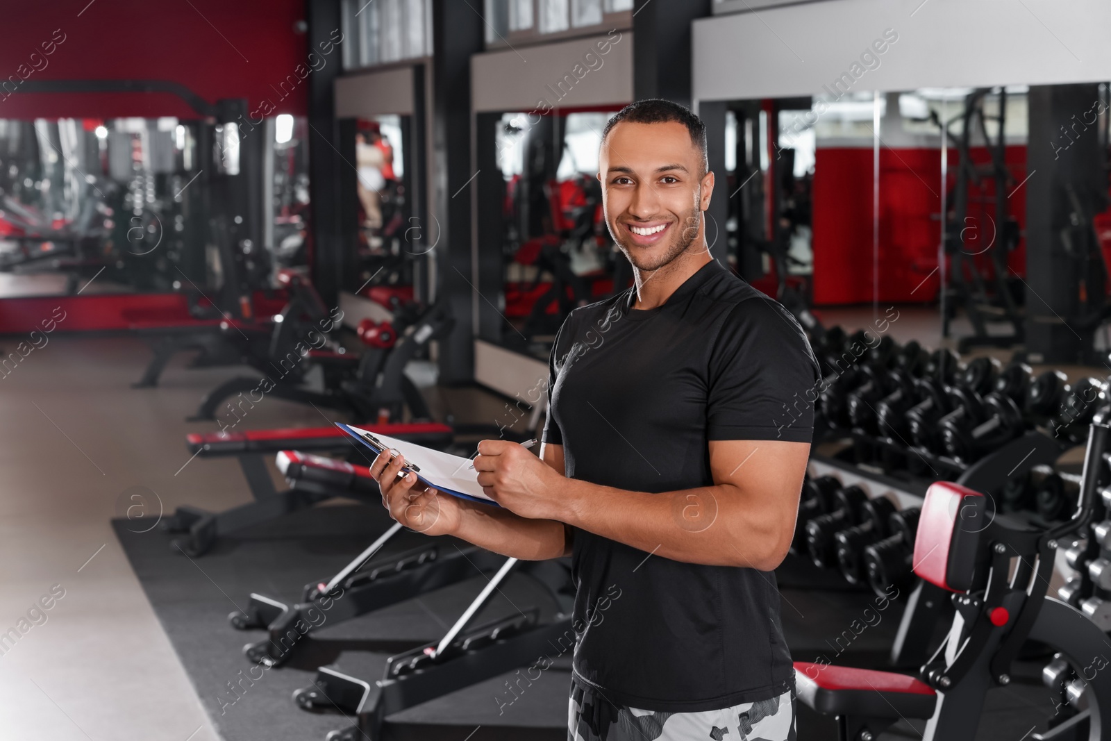 Photo of Happy trainer with workout plan in modern gym, space for text