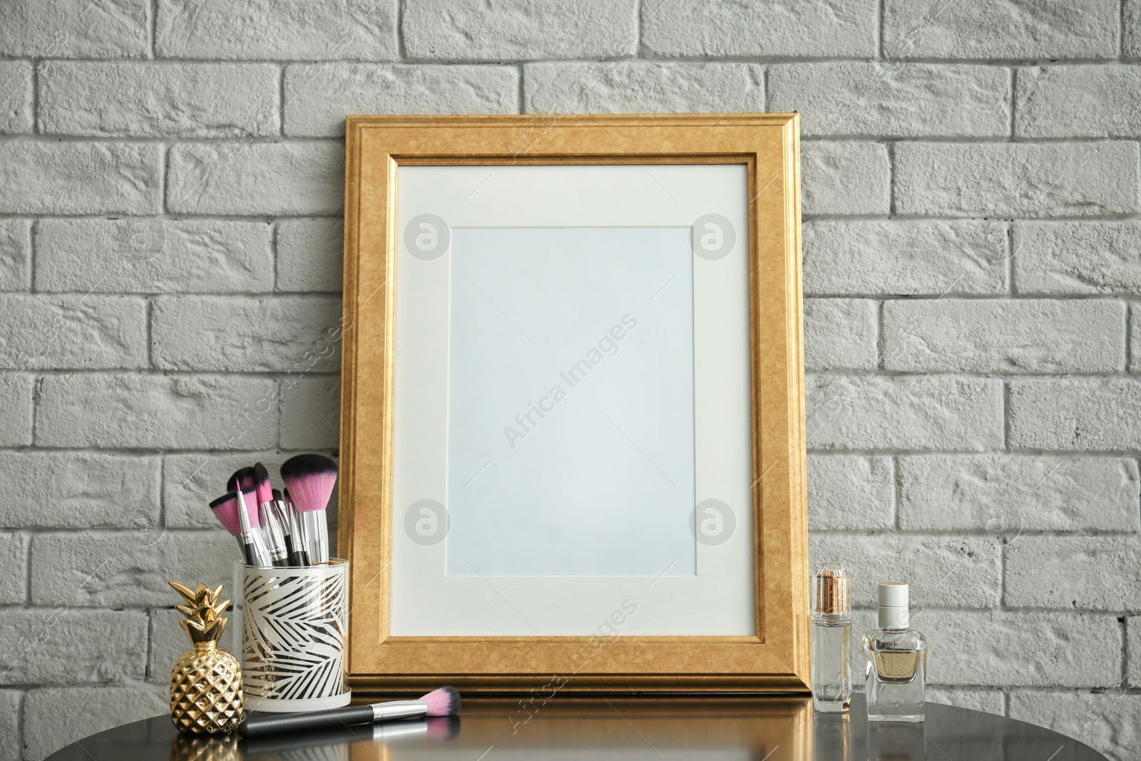 Photo of Mockup of blank frame and makeup brushes on table