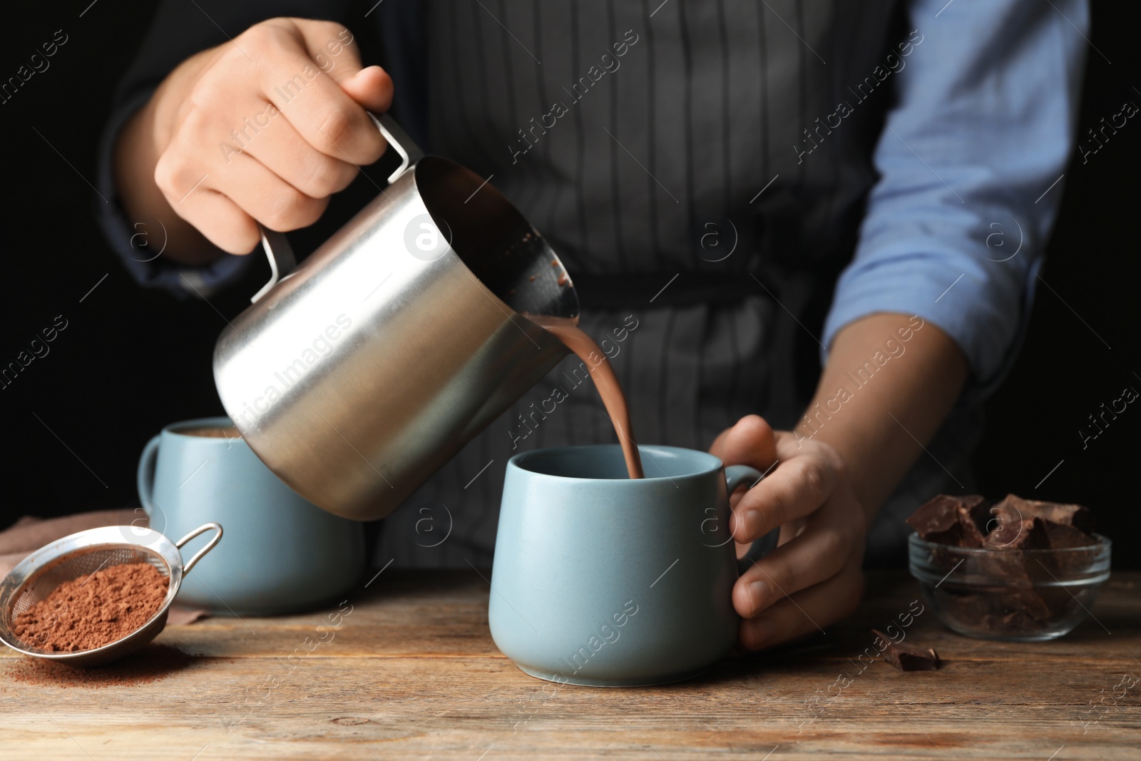 Photo of Woman pouring hot cocoa drink into cup on wooden table, closeup