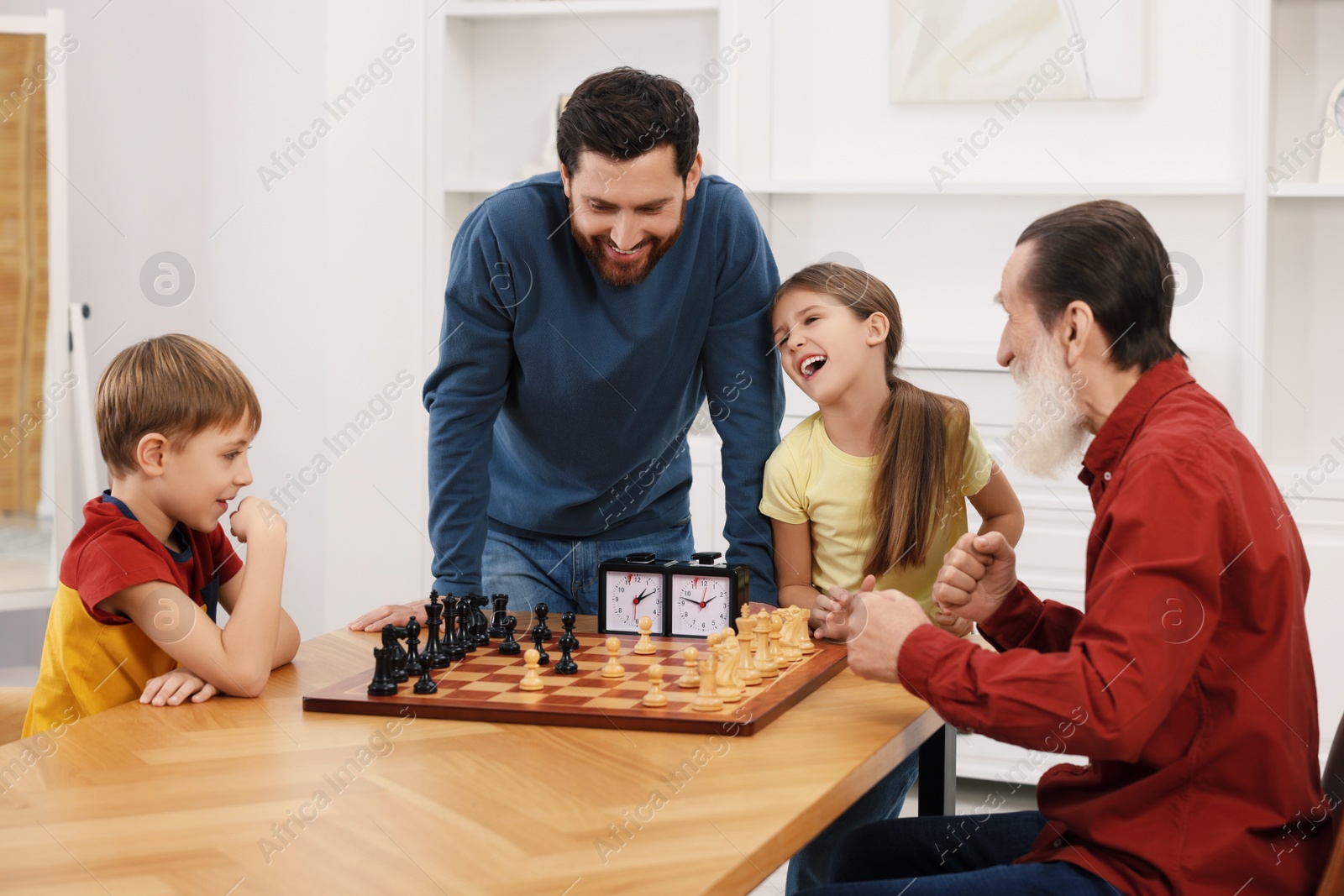 Photo of Family playing chess together at table in room