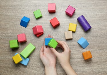 Photo of ABA therapist with colorful building blocks at wooden table, top view