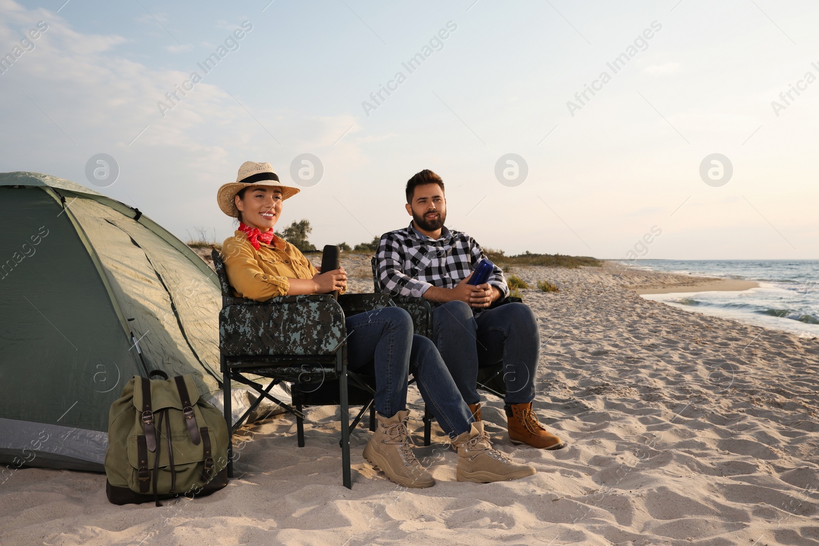 Photo of Couple with thermoses near camping tent on beach