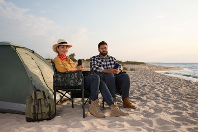 Photo of Couple with thermoses near camping tent on beach