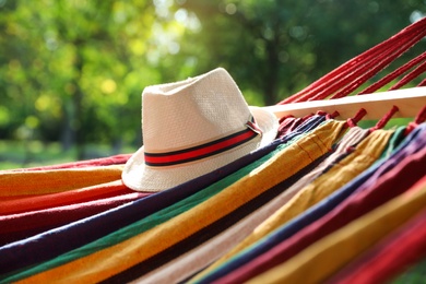 Photo of Bright comfortable hammock with hat hanging in green garden, closeup