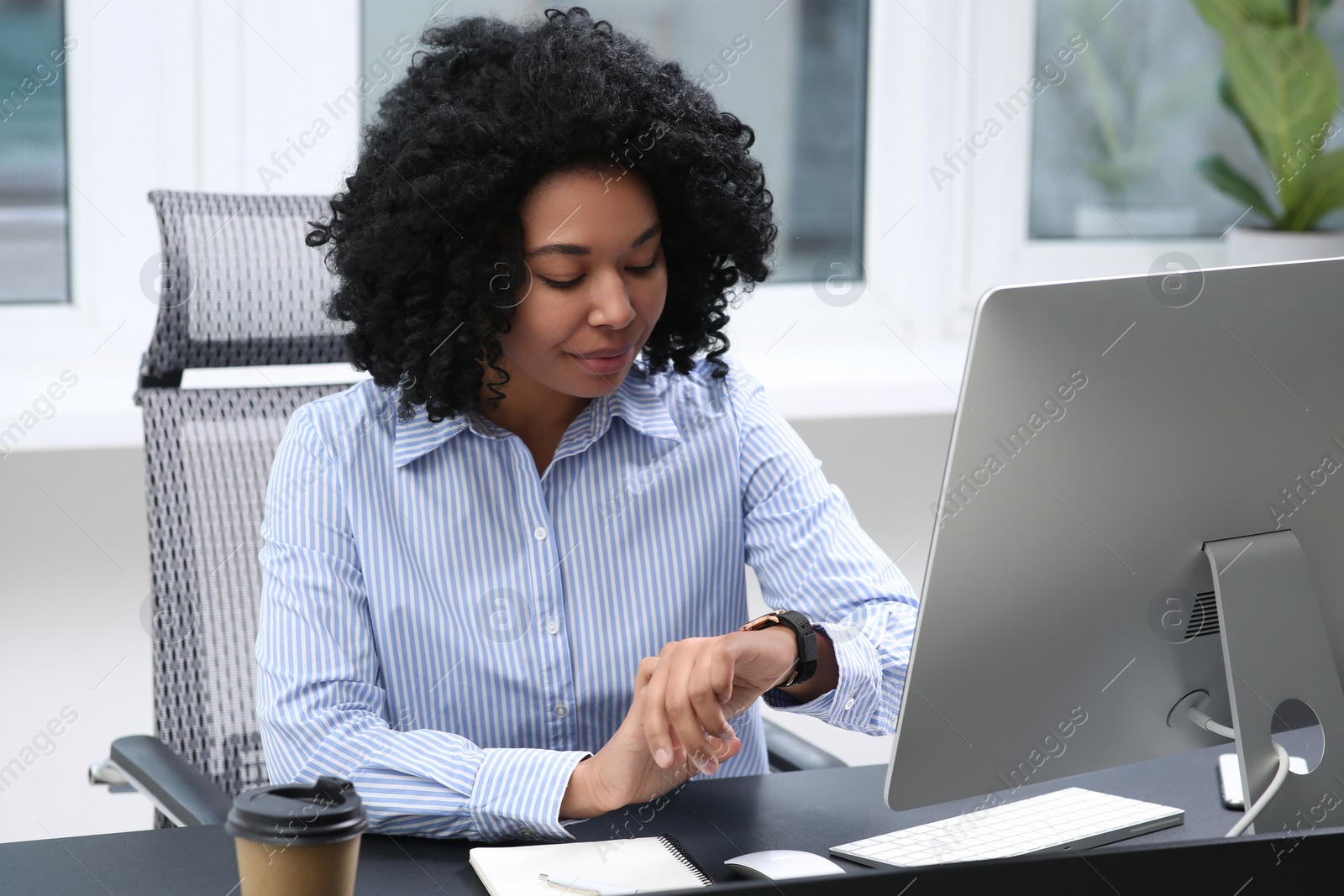 Photo of Young woman checking time on watch at table in office