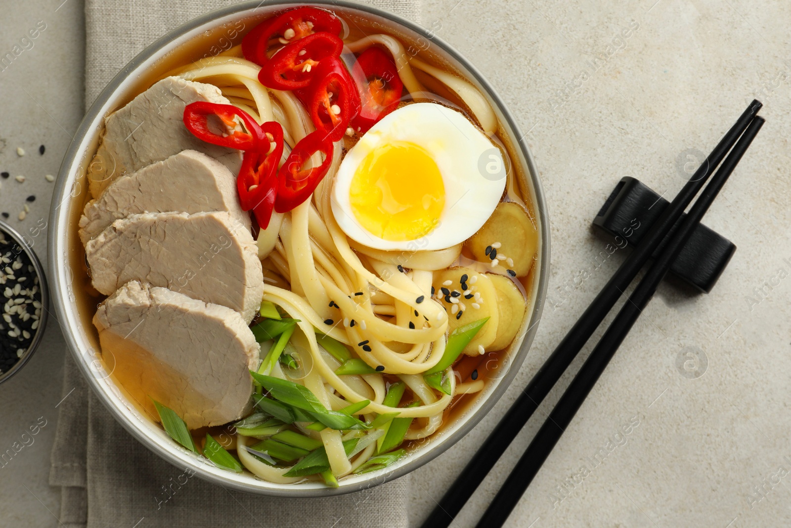 Photo of Delicious ramen in bowl and chopsticks on light textured table, flat lay. Noodle soup