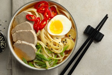 Photo of Delicious ramen in bowl and chopsticks on light textured table, flat lay. Noodle soup