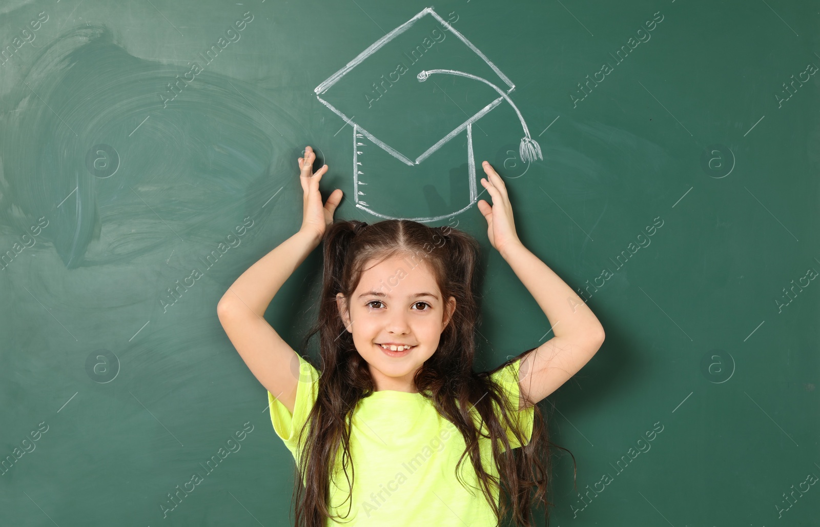 Photo of Little school child near chalkboard with drawing of graduate cap