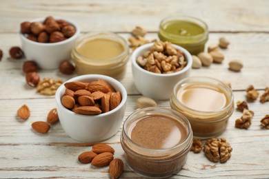 Photo of Jars with butters made of different nuts and ingredients on white wooden table, closeup