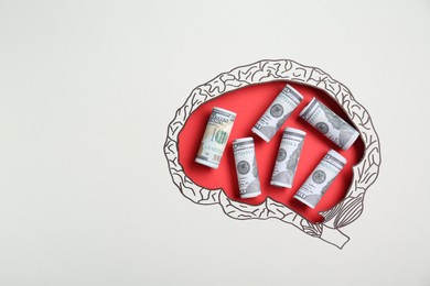 Photo of Rolled dollar banknotes on red background, top view through paper with brain shaped hole and drawing. Space for text