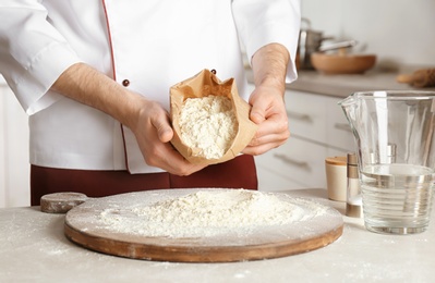 Photo of Male chef emptying flour out of paper package on board in kitchen