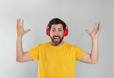 Emotional man listening music with headphones on light grey background