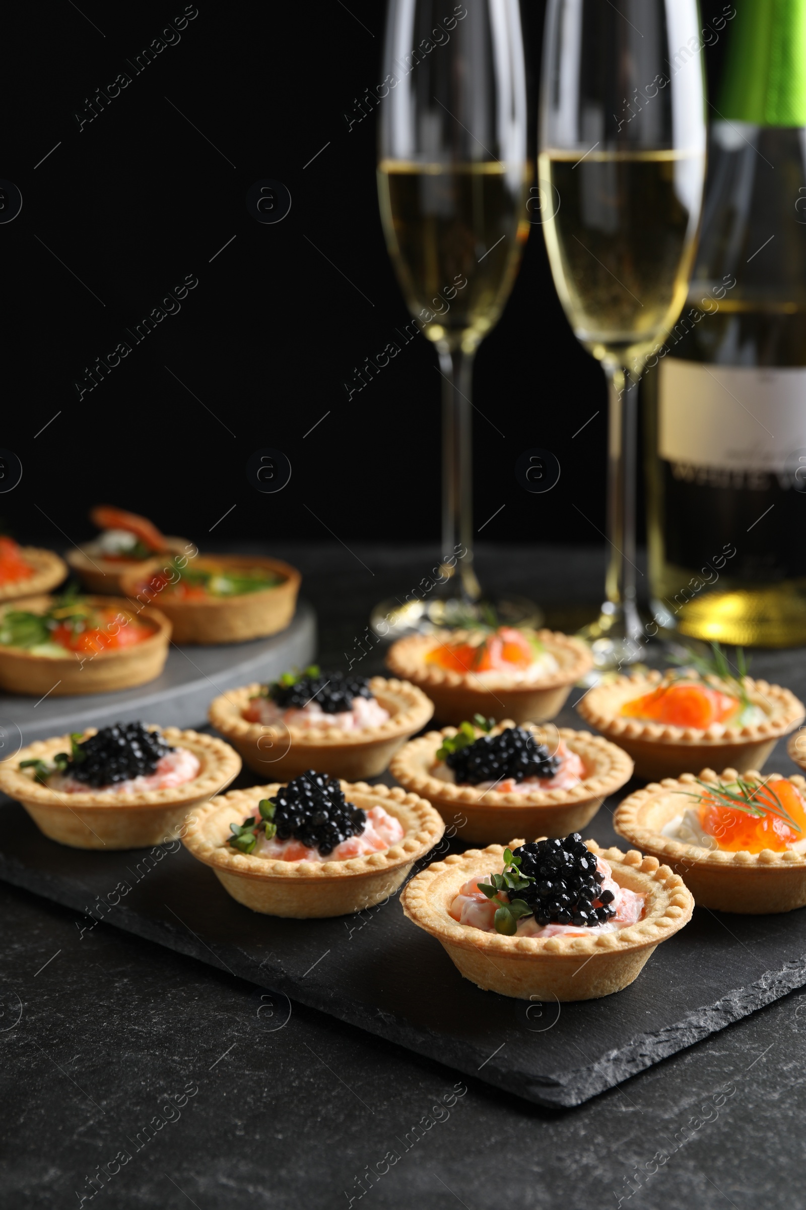 Photo of Delicious canapes with salmon and caviar on black textured table, closeup