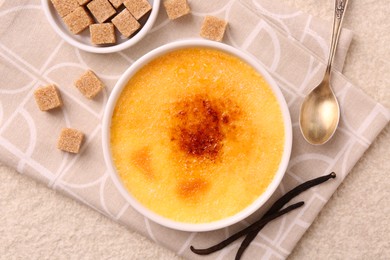 Photo of Delicious creme brulee in bowl, vanilla pods, sugar cubes and spoon on light textured table, top view