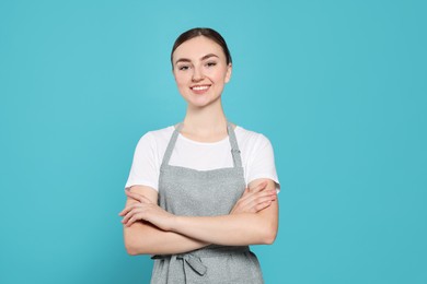 Beautiful young woman in clean apron with pattern on light blue background