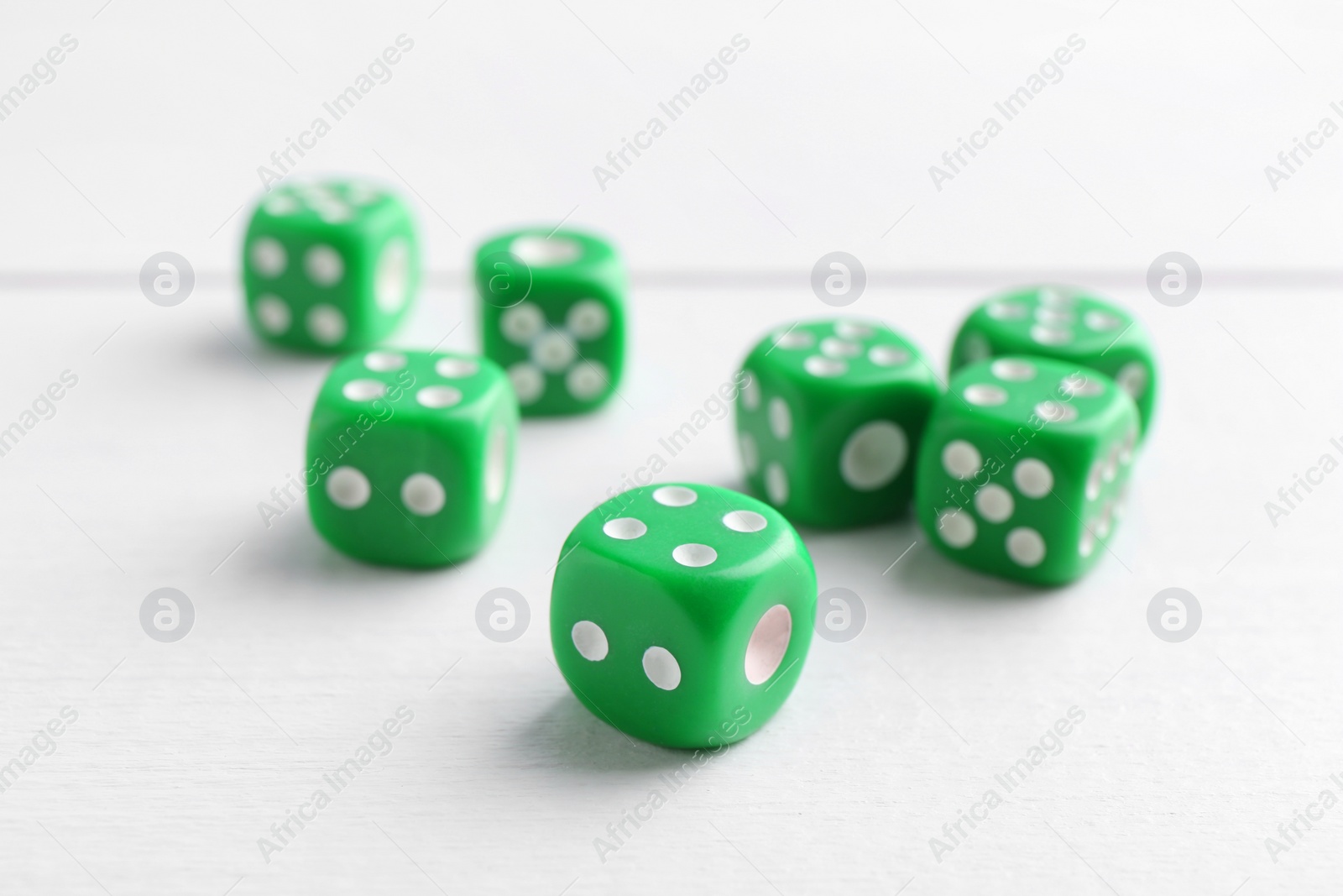 Photo of Many green game dices on white wooden table, closeup