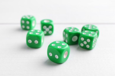 Many green game dices on white wooden table, closeup