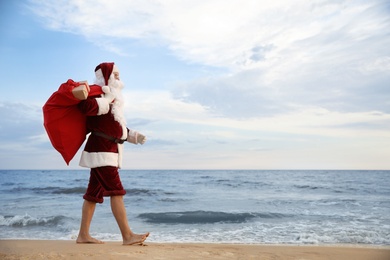 Photo of Santa Claus with bag of presents on beach, space for text. Christmas vacation