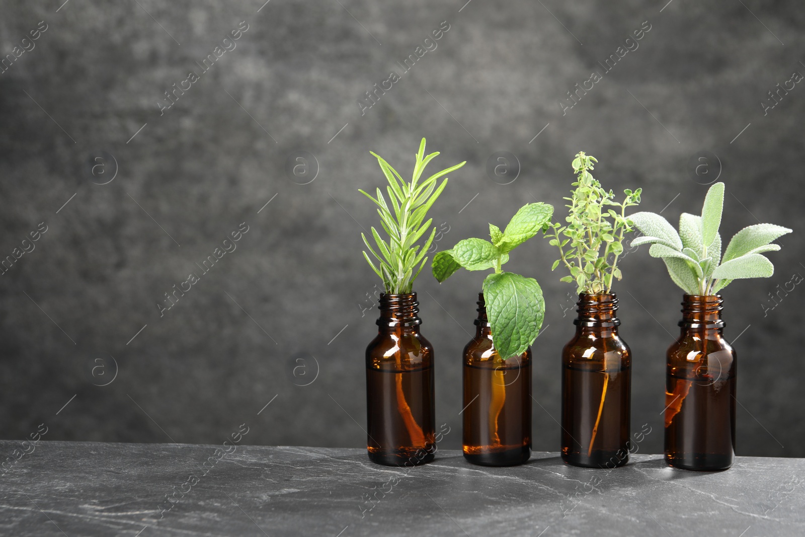 Photo of Bottles with essential oils and plants on grey textured table. Space for text