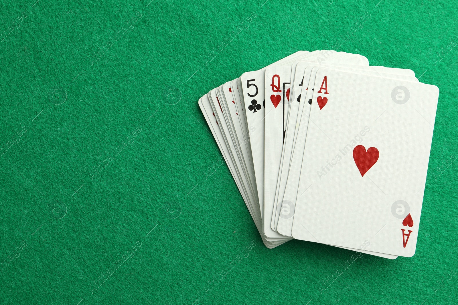 Photo of Deck of playing cards on green table, top view. Space for text