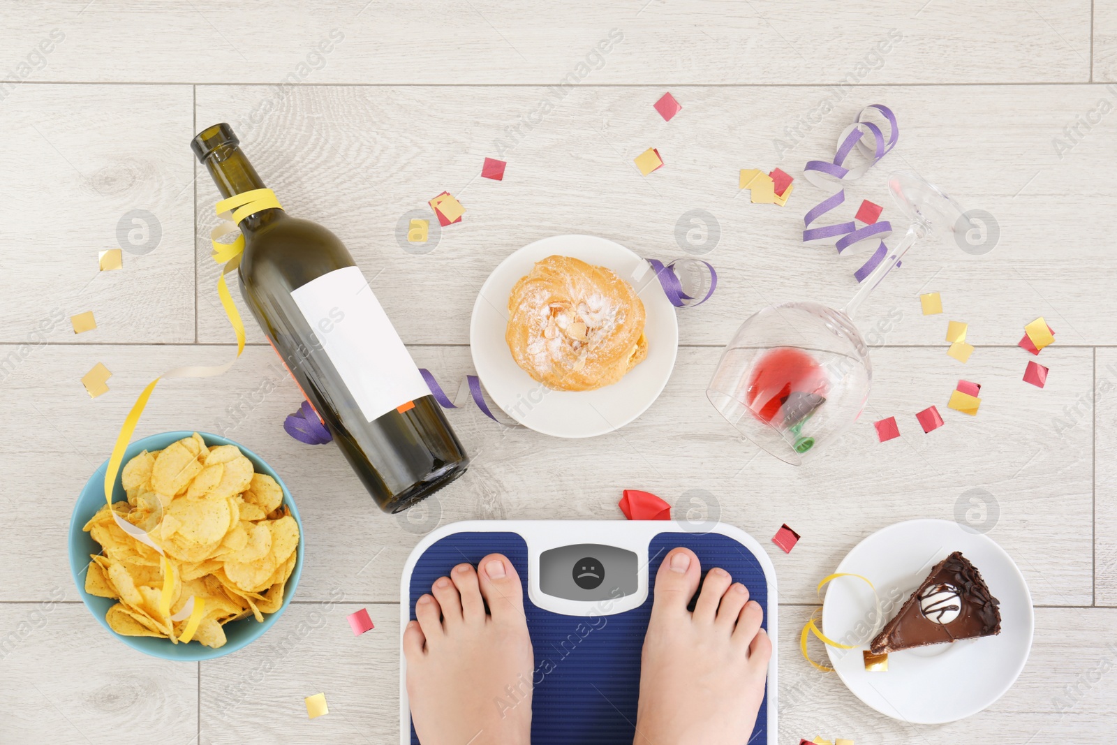 Photo of Woman standing on scales surrounded by different food and alcohol after party indoors, top view