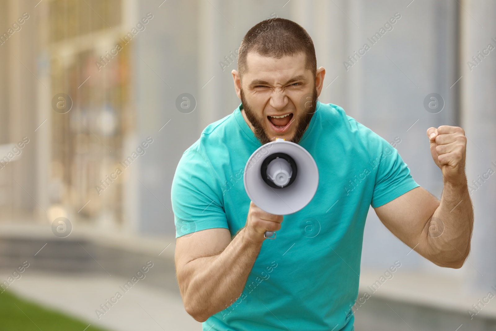 Image of Emotional young man with megaphone outdoors. Protest leader