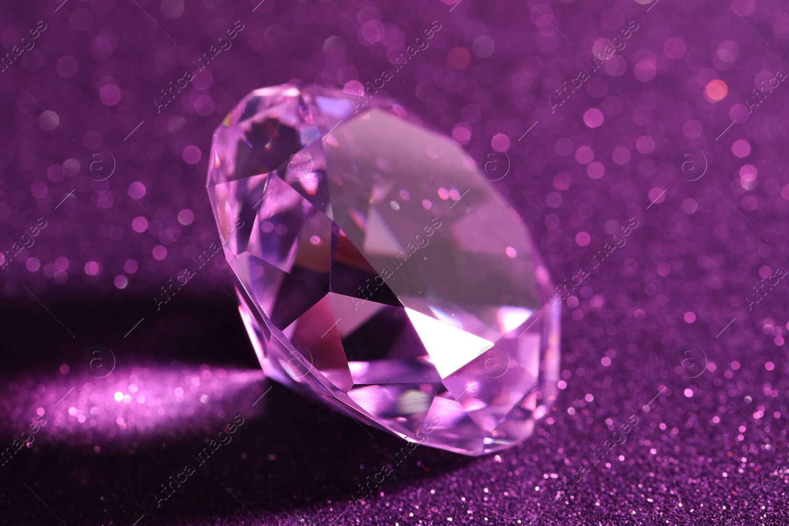 Photo of Beautiful shiny diamond on purple glitter background, closeup