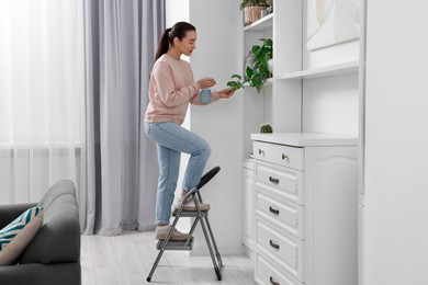 Woman on ladder watering houseplant at home