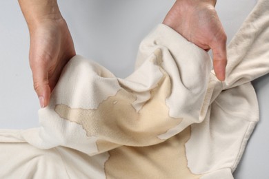 Photo of Woman holding beige sweater with stain on white background, closeup