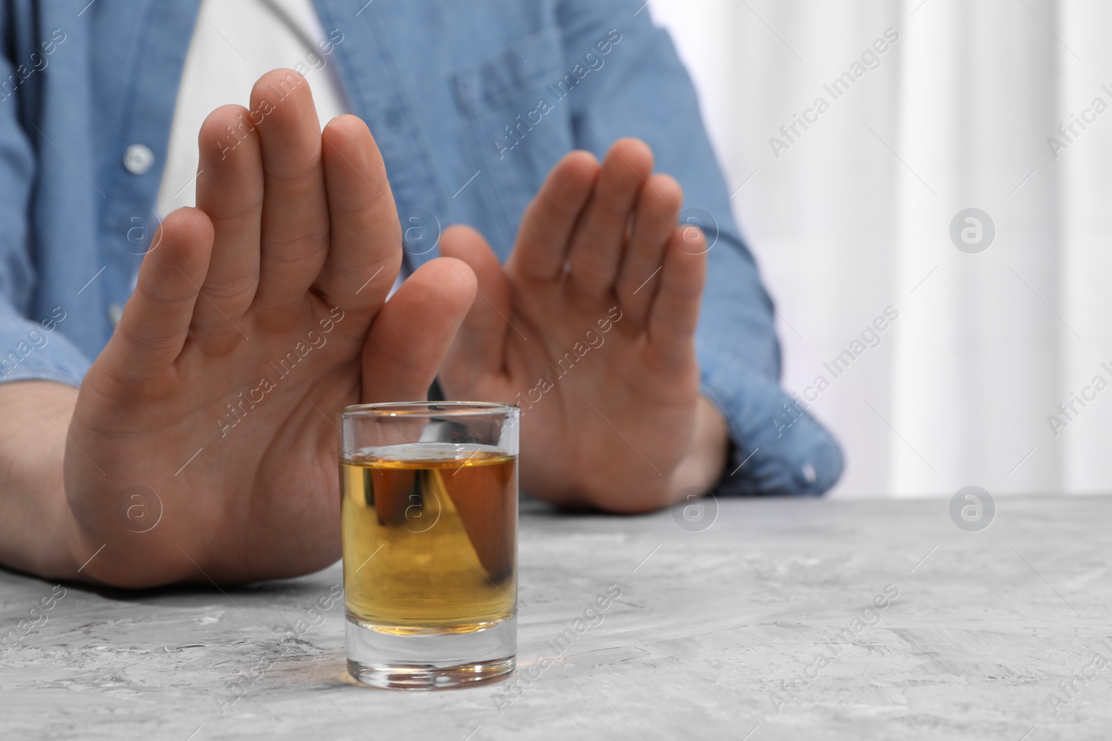 Photo of Alcohol addiction. Man refusing glass of whiskey at grey textured table indoors, closeup