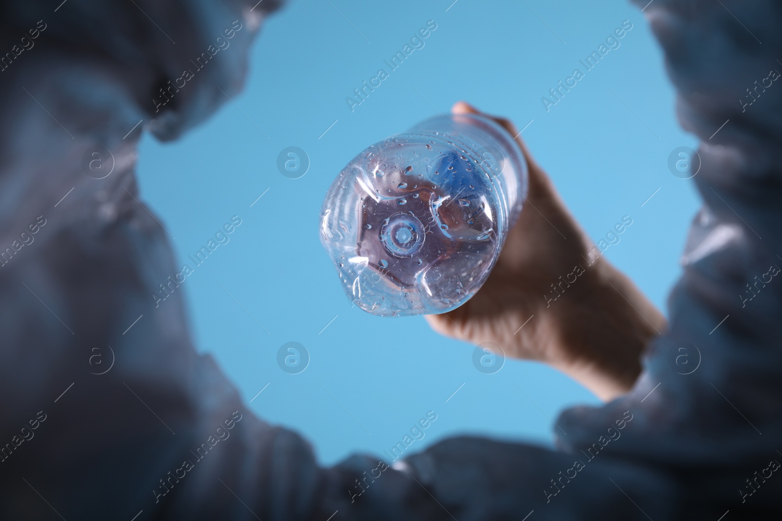 Photo of Bottom view of woman throwing plastic bottle into trash bin on light blue background, closeup