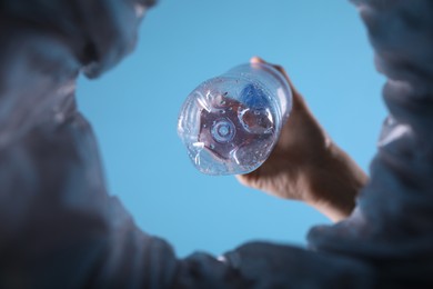 Photo of Bottom view of woman throwing plastic bottle into trash bin on light blue background, closeup