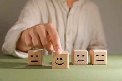 Photo of Choice concept. Woman choosing wooden cube with happy emoticon among others at green table, closeup