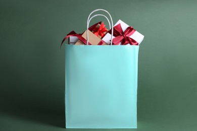 Photo of Turquoise paper shopping bag full of gift boxes on green background