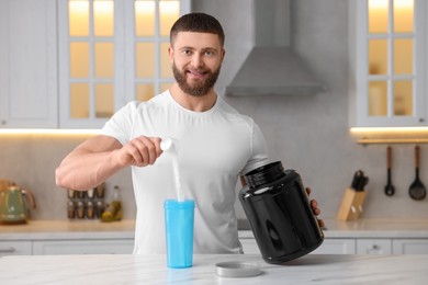 Photo of Young man making protein shake at white marble table in kitchen