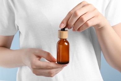 Photo of Woman holding bottle with serum against light grey background, closeup