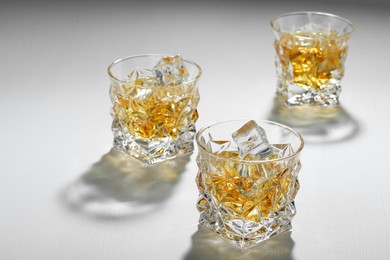 Photo of Whiskey with ice cubes in glasses on white table