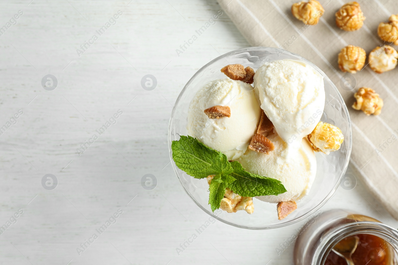 Photo of Delicious ice cream with caramel candies and popcorn in dessert bowl on white wooden table, flat lay. Space for text