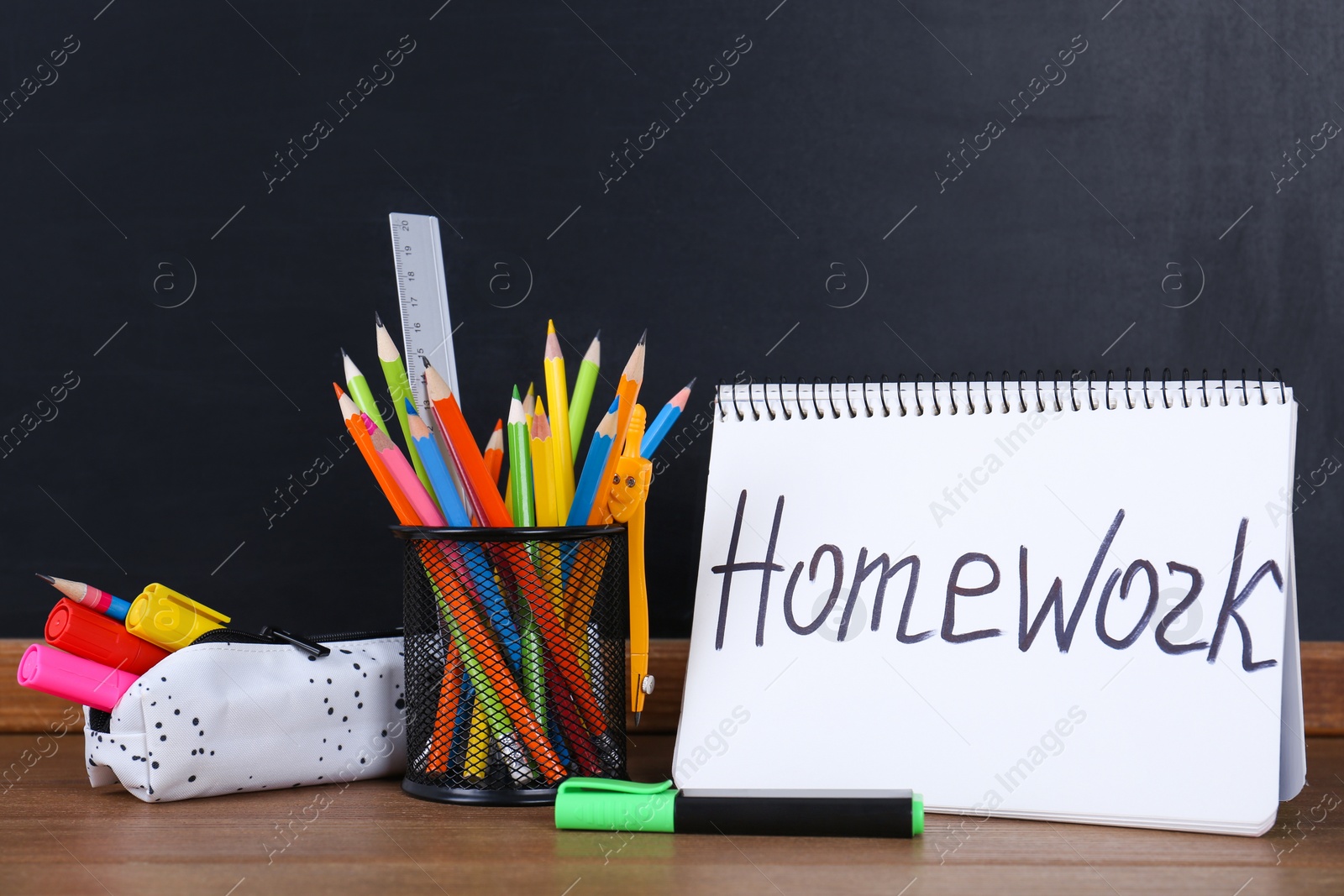 Photo of Stationery and notebook with inscription HOMEWORK on wooden table near blackboard