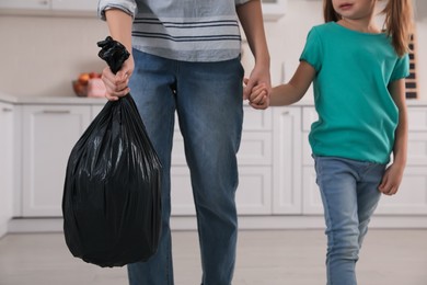 Woman holding bin bag full of garbage in kitchen, closeup