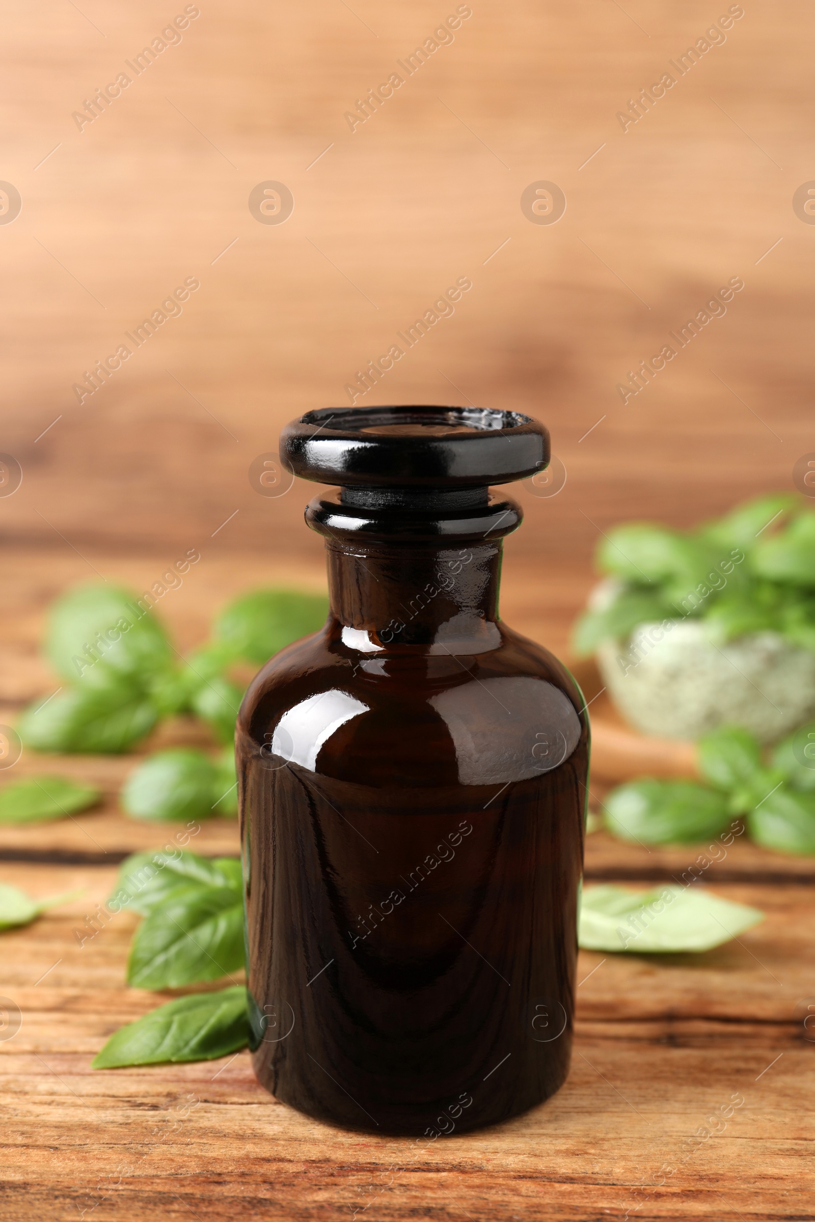 Photo of Glass bottle of basil essential oil and leaves on wooden table