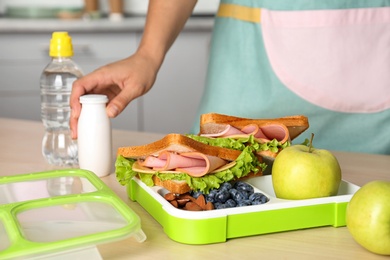 Woman preparing food for her child at table in kitchen, closeup. Healthy school lunch