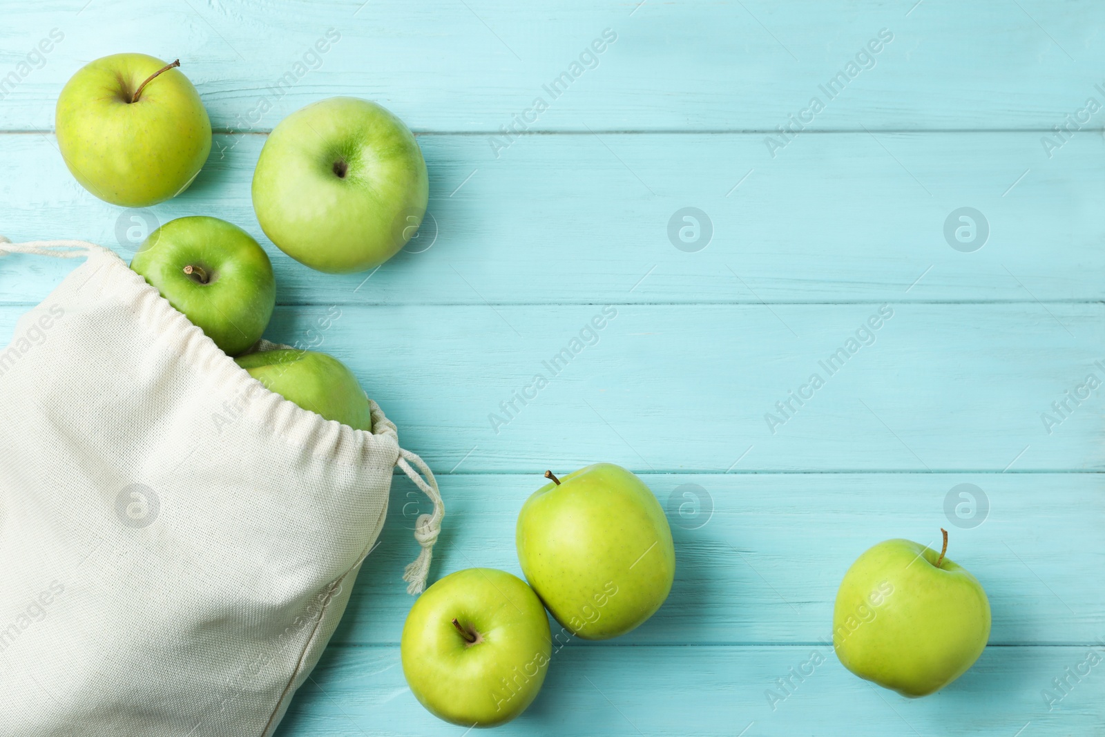 Photo of Cotton eco bag with apples on light blue wooden background, flat lay. Space for text