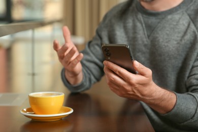 Photo of Handsome man with smartphone and cup of drink at table, closeup