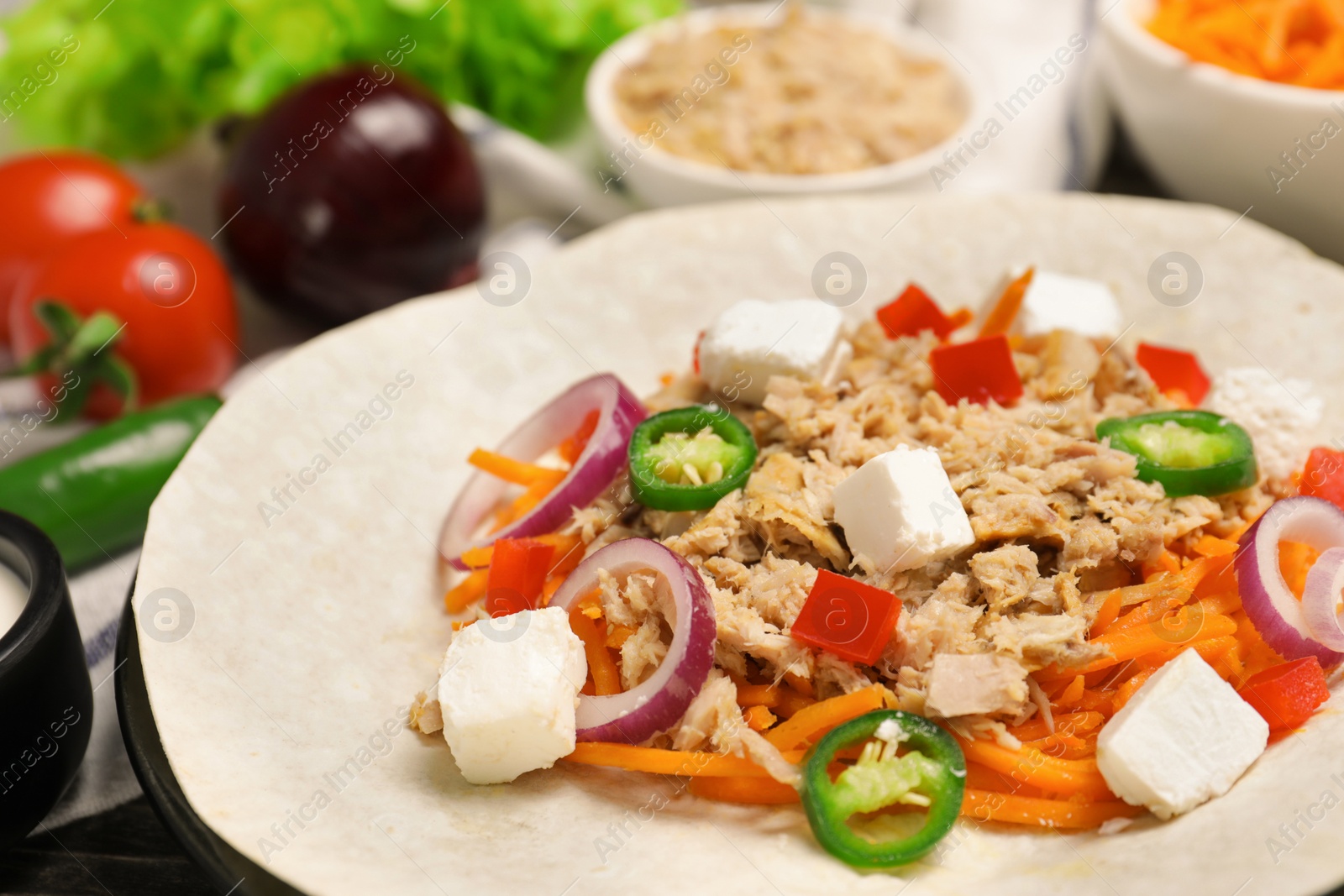 Photo of Delicious tortilla with tuna, vegetables and cheese on table, closeup. Cooking shawarma