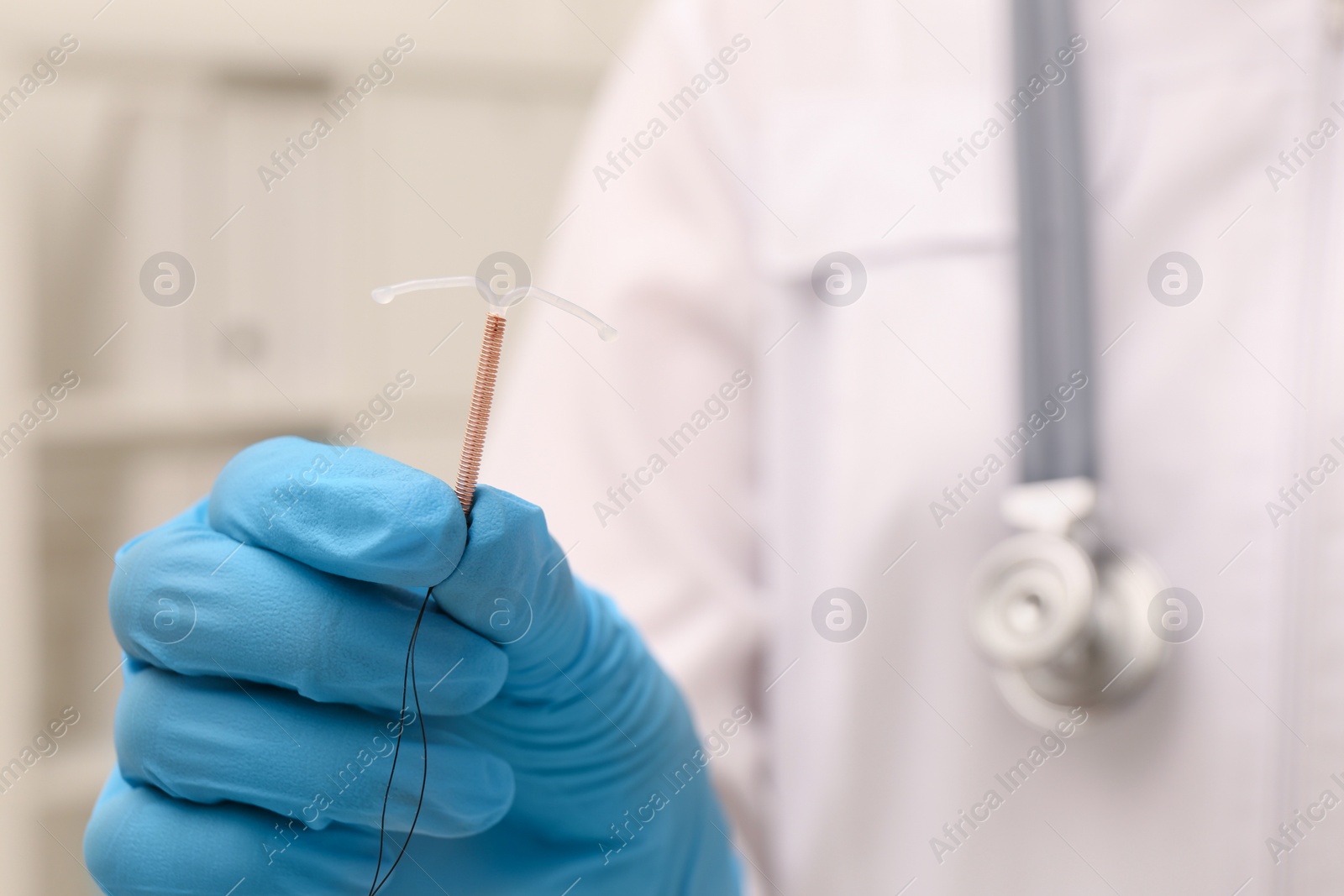 Photo of Doctor holding T-shaped intrauterine birth control device on blurred background, closeup. Space for text