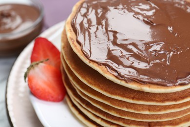 Photo of Tasty pancakes with chocolate paste and strawberries on table, closeup